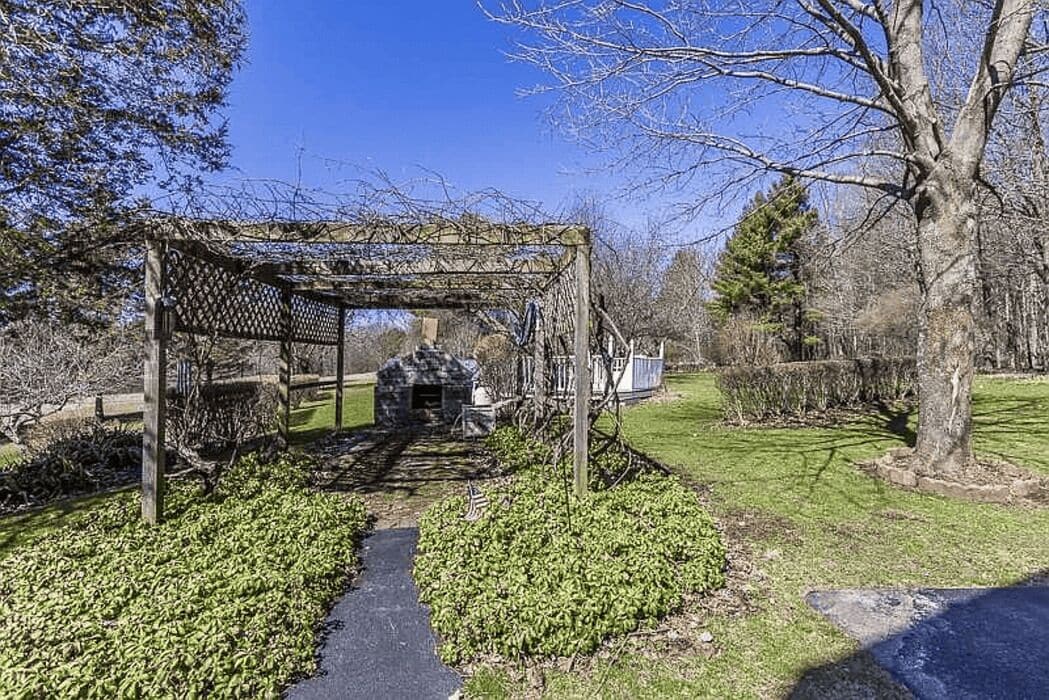 A gazebo with a lattice roof, surrounded by a stone wall and a pathway.