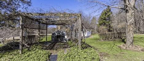A gazebo with a lattice roof, surrounded by a stone wall and a pathway.