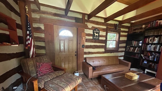 A log cabin interior with a wooden bench, a leather sofa, a coffee table, and a bookshelf.