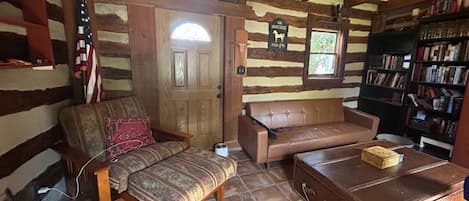 A log cabin interior with a wooden bench, a leather sofa, a coffee table, and a bookshelf.