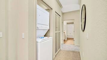 Un cuarto de lavado con lavadora y secadora, una puerta que da a otra habitación, y piso alfombrado.