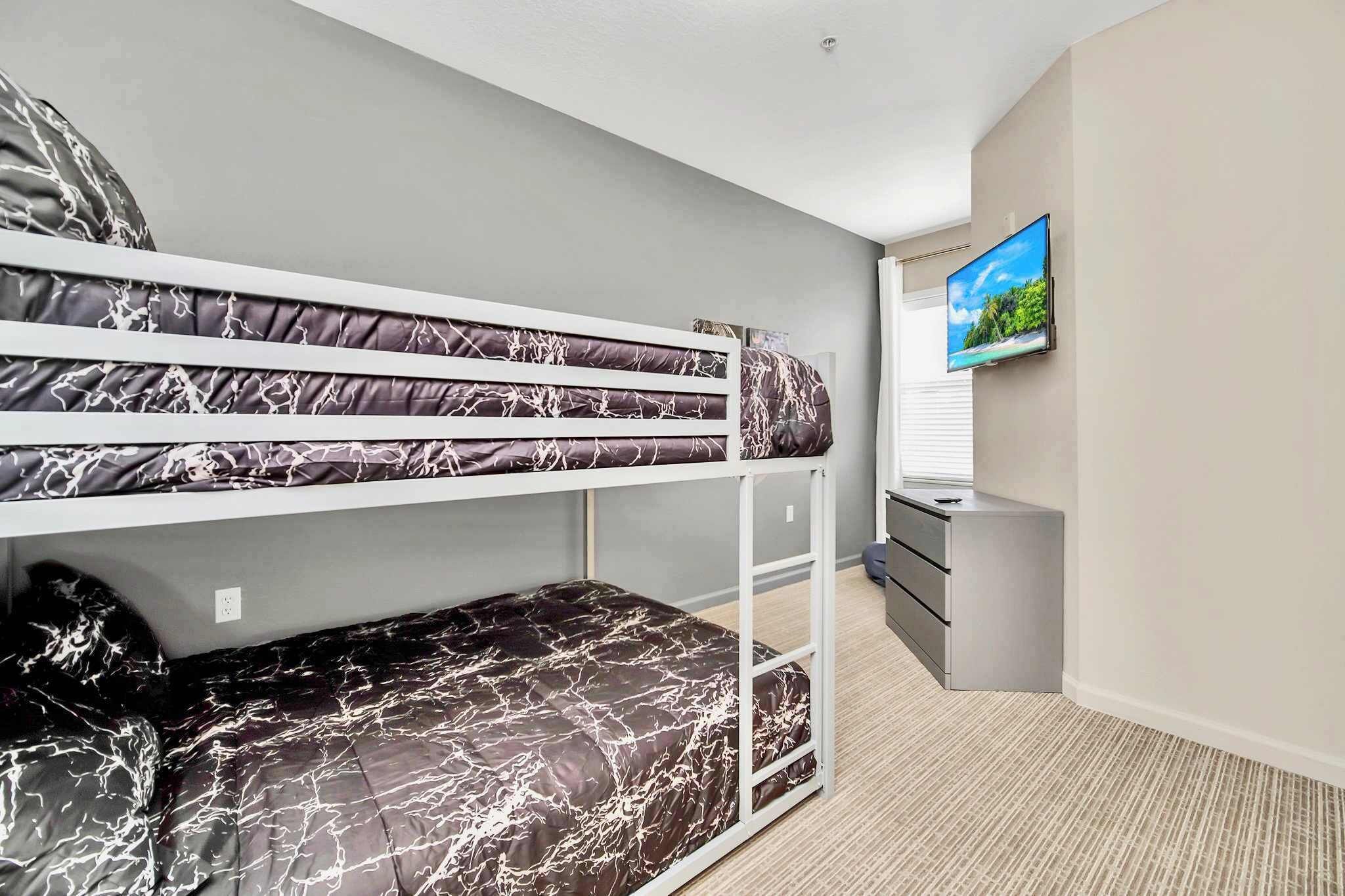A bunk bed with a TV on the wall, a small desk, and a window.