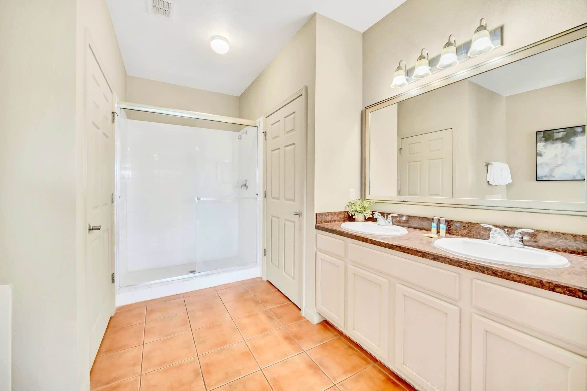 A bathroom with two sinks, a large mirror, and a shower.