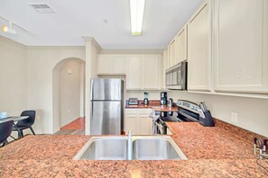 Una cocina con encimeras de granito, electrodomésticos de acero inoxidable y armarios blancos.