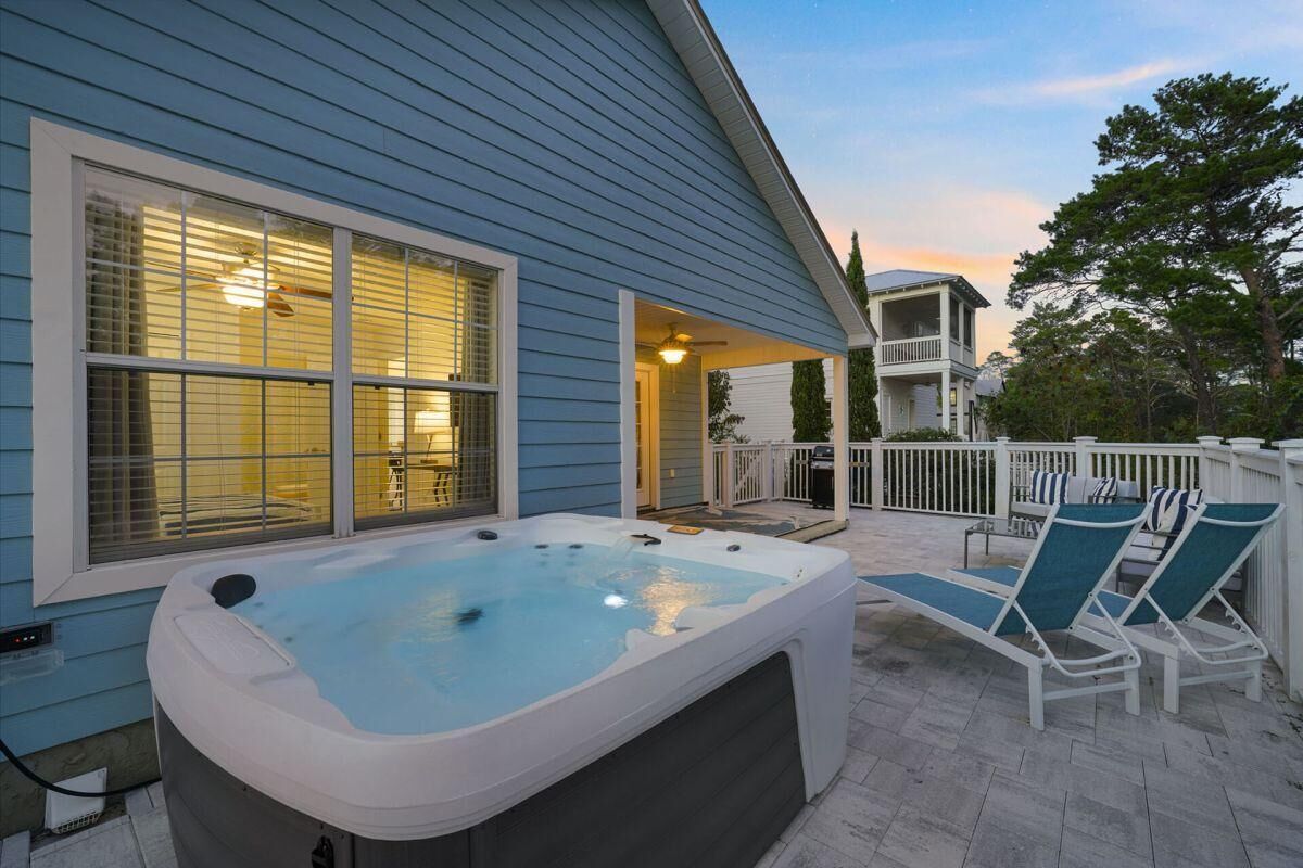 A hot tub outside a house with a covered patio area and lounge chairs.