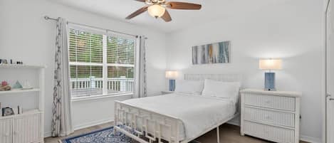 A bedroom with a bed, nightstands, a ceiling fan, a window with curtains, and a patterned rug.