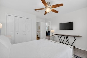 Ein Schlafzimmer mit einem Bett, einem Deckenventilator, einem an der Wand befestigten Fernseher und einem Nachttisch mit Lampe.