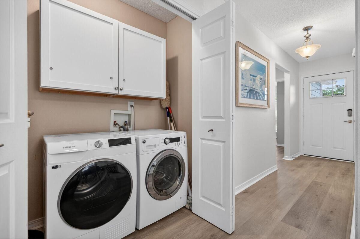 Een wasserette met twee witte wasmachines en drogers, een witte deur en een gang naar een andere kamer.