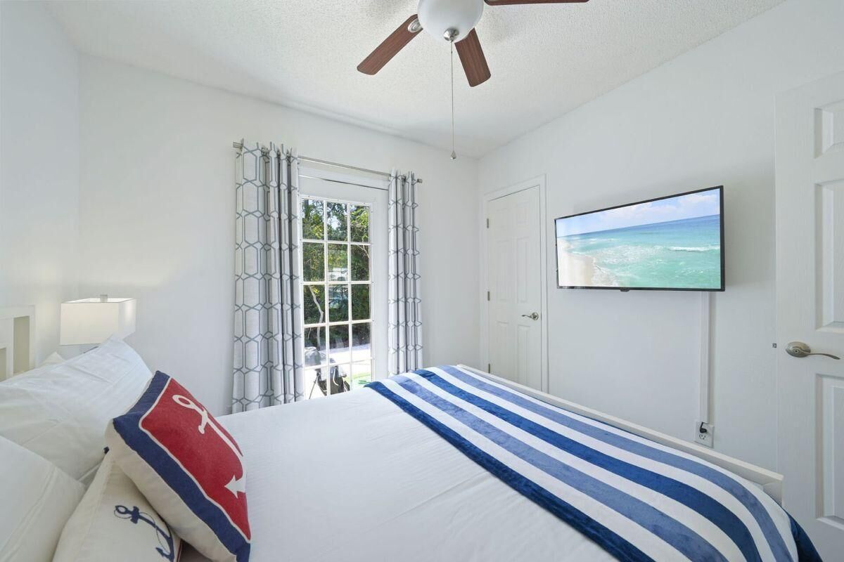 Una habitación de hotel con una cama, ventilador de techo, televisión y ventana con cortinas.