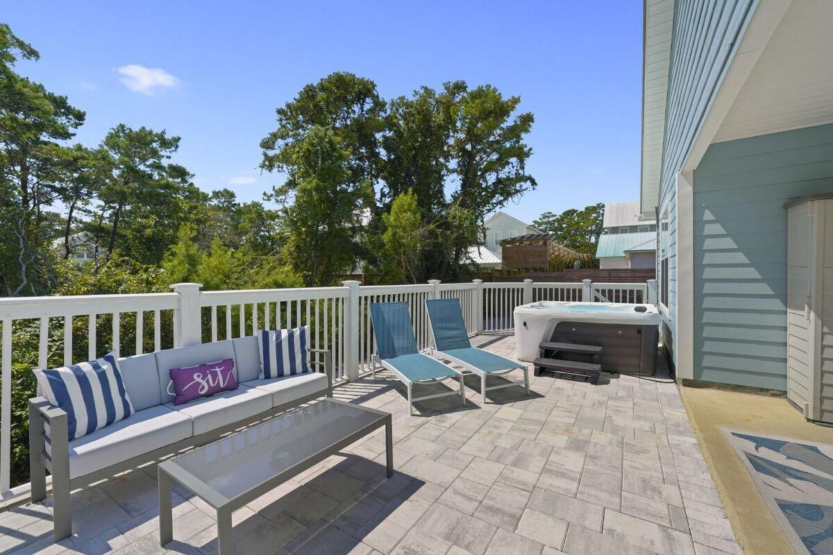 An outdoor patio with a white deck, a seating area with a bench and lounge chairs, and a hot tub.