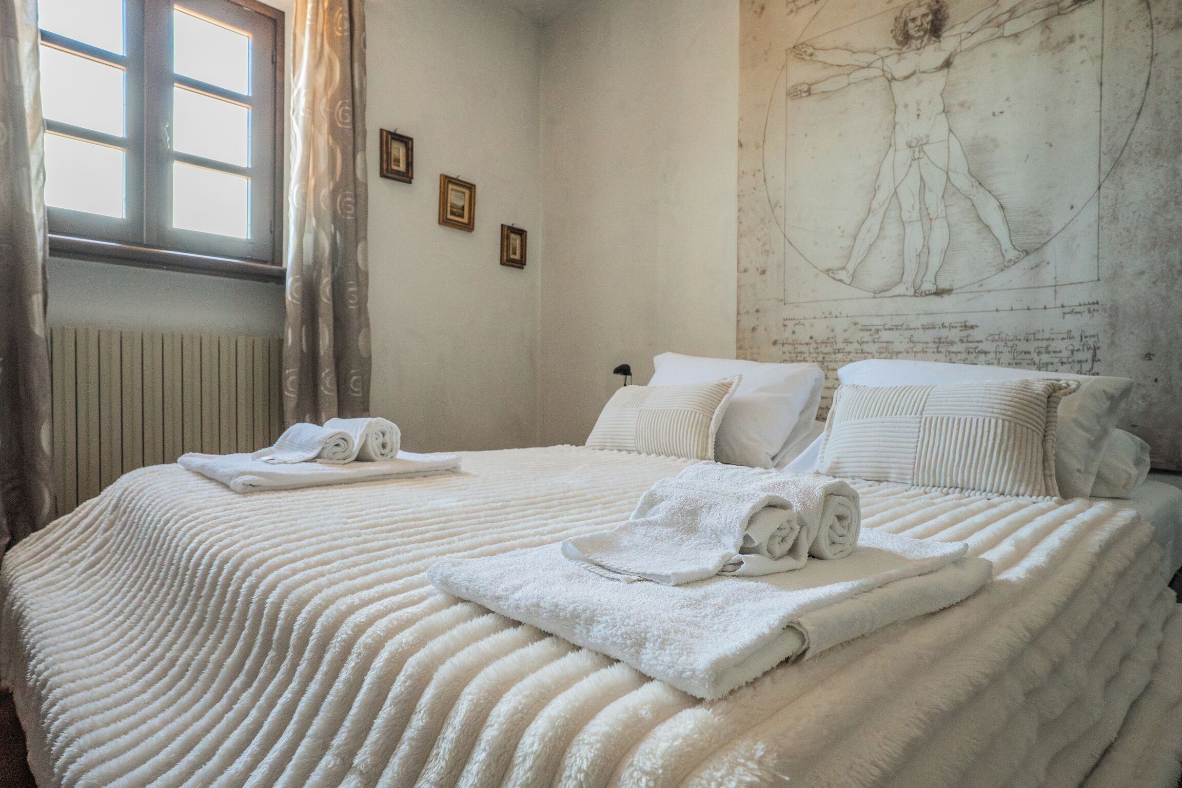 A room with a bed, towels, a window, and a wall with a drawing.