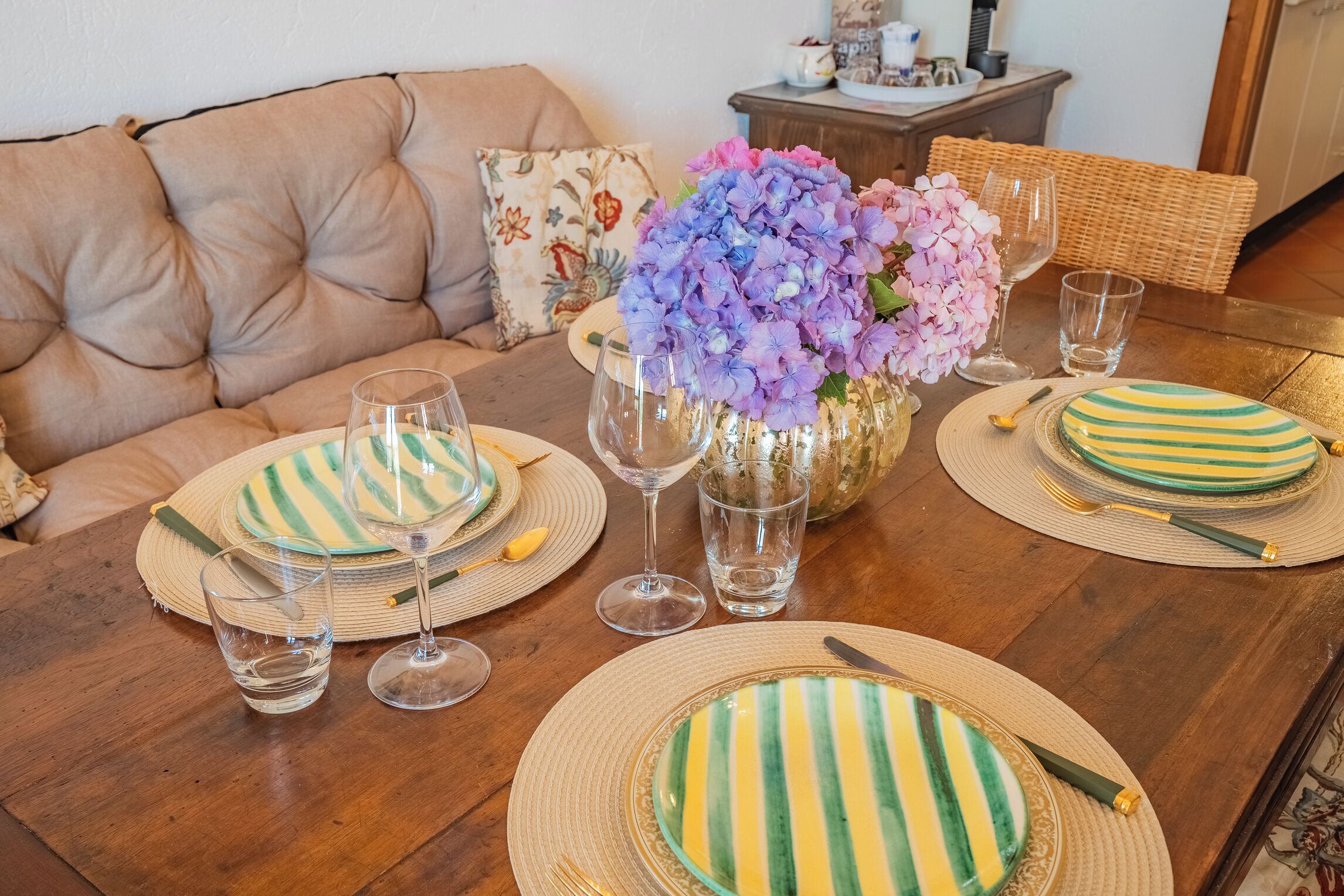 A dining table set with striped plates, clear glasses, and a vase of flowers.