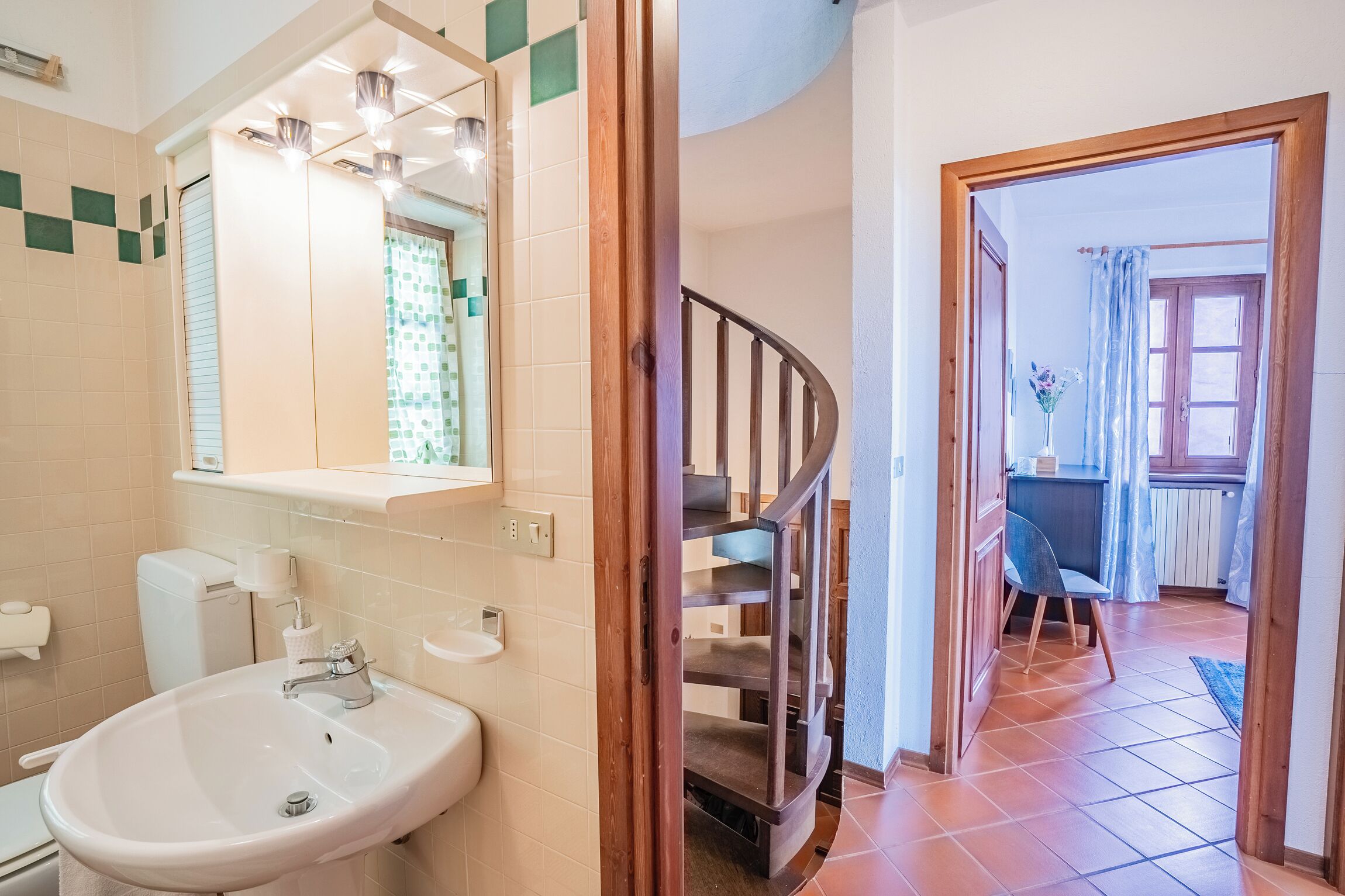 A bathroom with a sink, toilet, and mirror. There is a staircase leading to a dining area with a table and chairs.