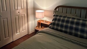 A bedroom with a bed, a nightstand, a lamp, and a closed door. - Gig'em Getaway Pool House - Sleeps 10 (Bryan)