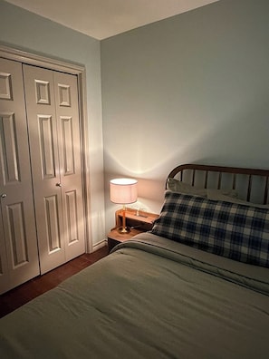 A bedroom with a bed, a nightstand, a lamp, and a closed door. - Gig'em Getaway Pool House - Sleeps 10 (Bryan)