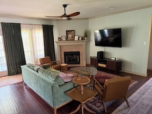 A living room with a sofa, chairs, a coffee table, a fireplace, a television, and a ceiling fan. - Gig'em Getaway Pool House - Sleeps 10 (Bryan)