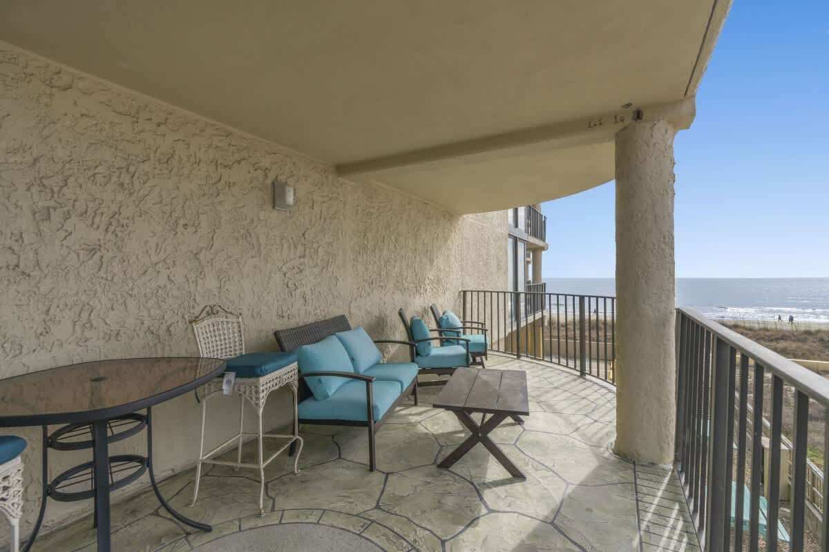 Een overdekt terras met een tafel, stoelen en een bank, met uitzicht op het strand.