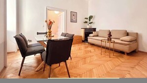 A modern living room with a dining area, featuring a herringbone floor pattern, a sofa, a coffee table, and a pendant light. - Servus Homes - rooftop terrace & balcony - Metro (Vienna)