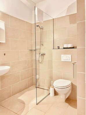 Een moderne badkamer met een glazen douchecabine, toilet en wastafel.