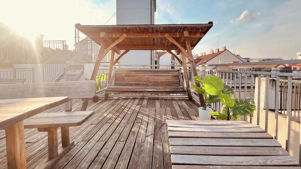 A wooden deck with a covered seating area, surrounded by railings and potted plants. - Servus Homes - rooftop terrace & balcony - Metro (Vienna)