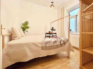 Een slaapkamer met een bed, nachtkastje, lamp en een raam met uitzicht.
