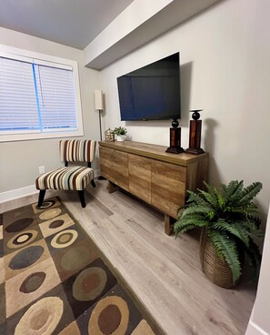 Un salon avec un téléviseur fixé au mur, un fauteuil à rayures, un meuble en bois et un tapis à motifs.