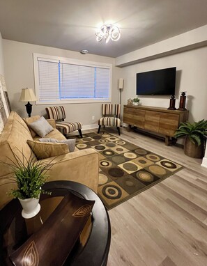 A living room with a sofa, chairs, a coffee table, a TV, and a patterned rug. - Modern 2BR Retreat | Fully Equipped | 31+ Day Stays — minutes to downtown Ottawa (Ottawa)