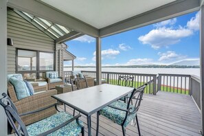 A covered outdoor deck with a table and chairs, overlooking a body of water and distant hills. - Bernard's Best - Spacious 4-bedroom townhome on Smith Mt Lake (Moneta)