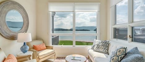 Una sala de estar con vistas a un lago y montañas, amoblada con un sofá, sillones y una mesa de centro.