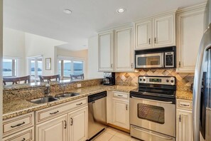 Cozinha com bancadas de granito, eletrodomésticos de aço inoxidável e armários brancos.