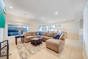 A spacious living room with a sectional sofa, a coffee table, and a large window providing natural light. - Bernard's Best - Spacious 4-bedroom townhome on Smith Mt Lake (Moneta)