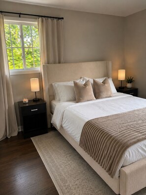 Ein Schlafzimmer mit einem großen Bett, zwei Nachttischen, einem Fenster mit Vorhängen und Blick auf Grünfläche.