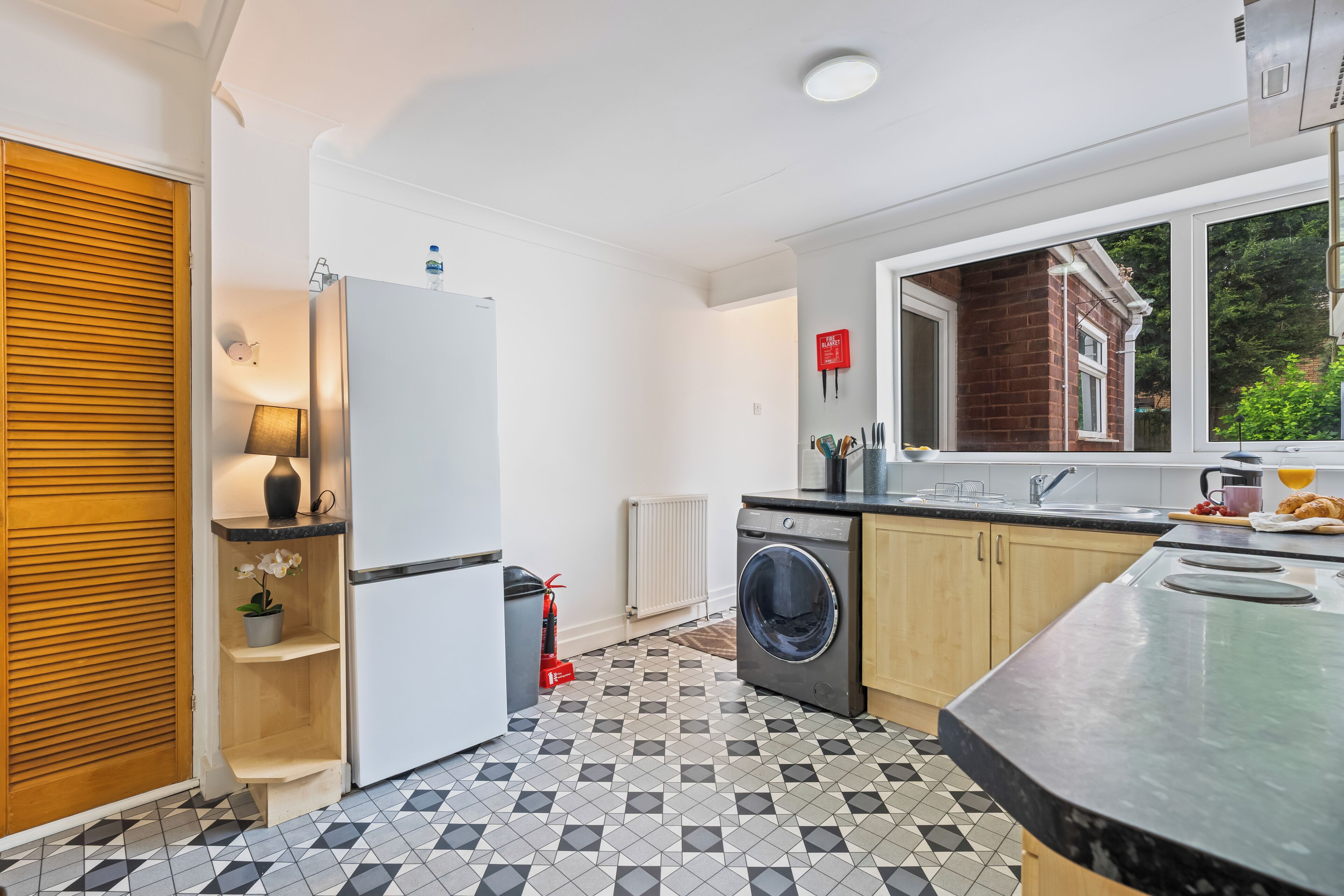 A modern kitchen with a refrigerator, washing machine, and a window with a view of a brick building.