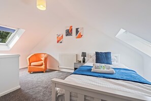 A bedroom with a sloped ceiling, a bed with a blue blanket, an orange armchair, a radiator, and artwork on the wall. - Contractor Accommodation in Cannock - Sleeps 5 (Cannock)