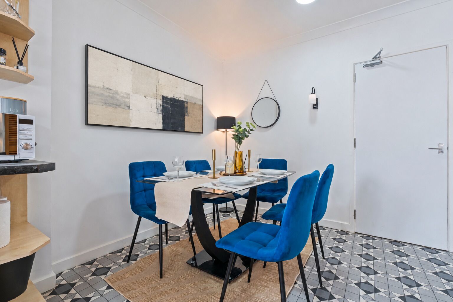 A dining area with a table set for four, blue chairs, a modern lamp, and a painting on the wall.