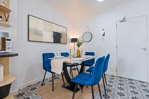 A dining area with a table set for four, blue chairs, a modern lamp, and a painting on the wall. - Contractor Accommodation in Cannock - Sleeps 5 (Cannock)