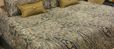 A bed with a patterned bedspread, pillows, and a bedside lamp.