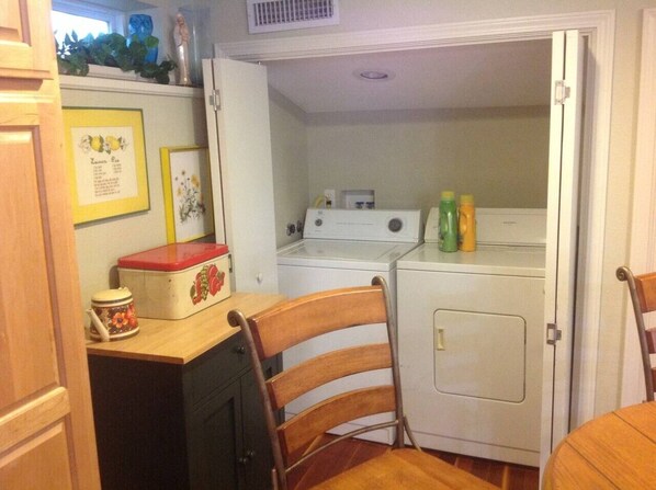 A compact kitchen with a washing machine, a table with a chair, and a refrigerator.