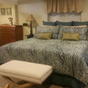 A bedroom with a bed, a nightstand, a lamp, a dresser, and a window with curtains.