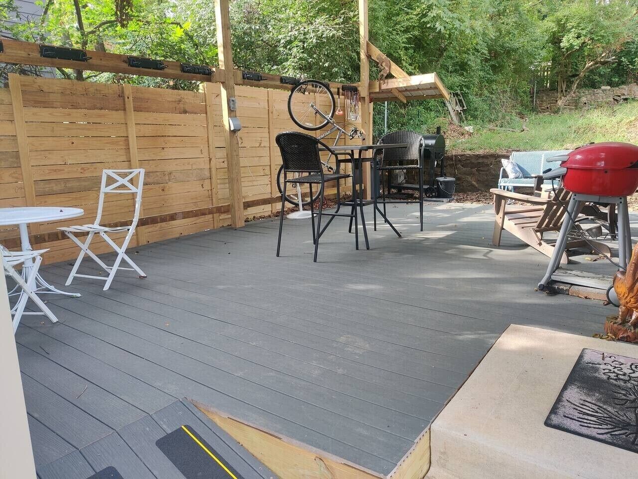 A covered patio with a wooden deck, a table and chairs, a grill, and a bicycle.