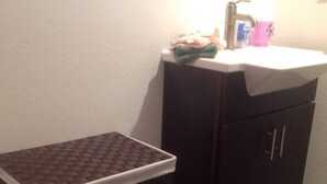 A bathroom with a dark wooden cabinet, a white sink, and a small tiled stool. - Downtown Bohemian Bungalow Full Bed Bottom TwinTop (Fayetteville)
