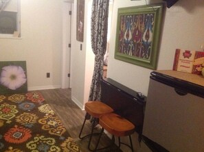 A compact kitchen with a refrigerator, a microwave, and a small table with two stools. - Downtown Bohemian Bungalow Full Bed Bottom TwinTop (Fayetteville)
