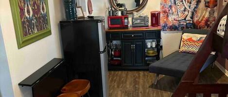 A compact living space with a kitchenette, a flat-screen TV, a coffee machine, and a patterned rug.