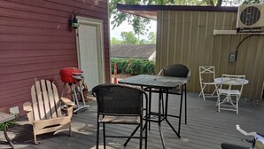 A wooden deck with outdoor furniture including a table and chairs, a grill, and a small table with a chair. - Downtown Bohemian Bungalow Full Bed Bottom TwinTop (Fayetteville)