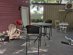 A wooden deck with outdoor furniture including a table and chairs, a grill, and a small table with a chair. - Downtown Bohemian Bungalow Full Bed Bottom TwinTop (Fayetteville)