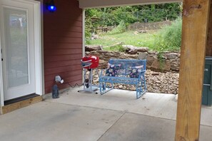 A covered patio area with a grill, a blue metal bench, and a stone wall in the background. - Downtown Bohemian Bungalow Full Bed Bottom TwinTop (Fayetteville)