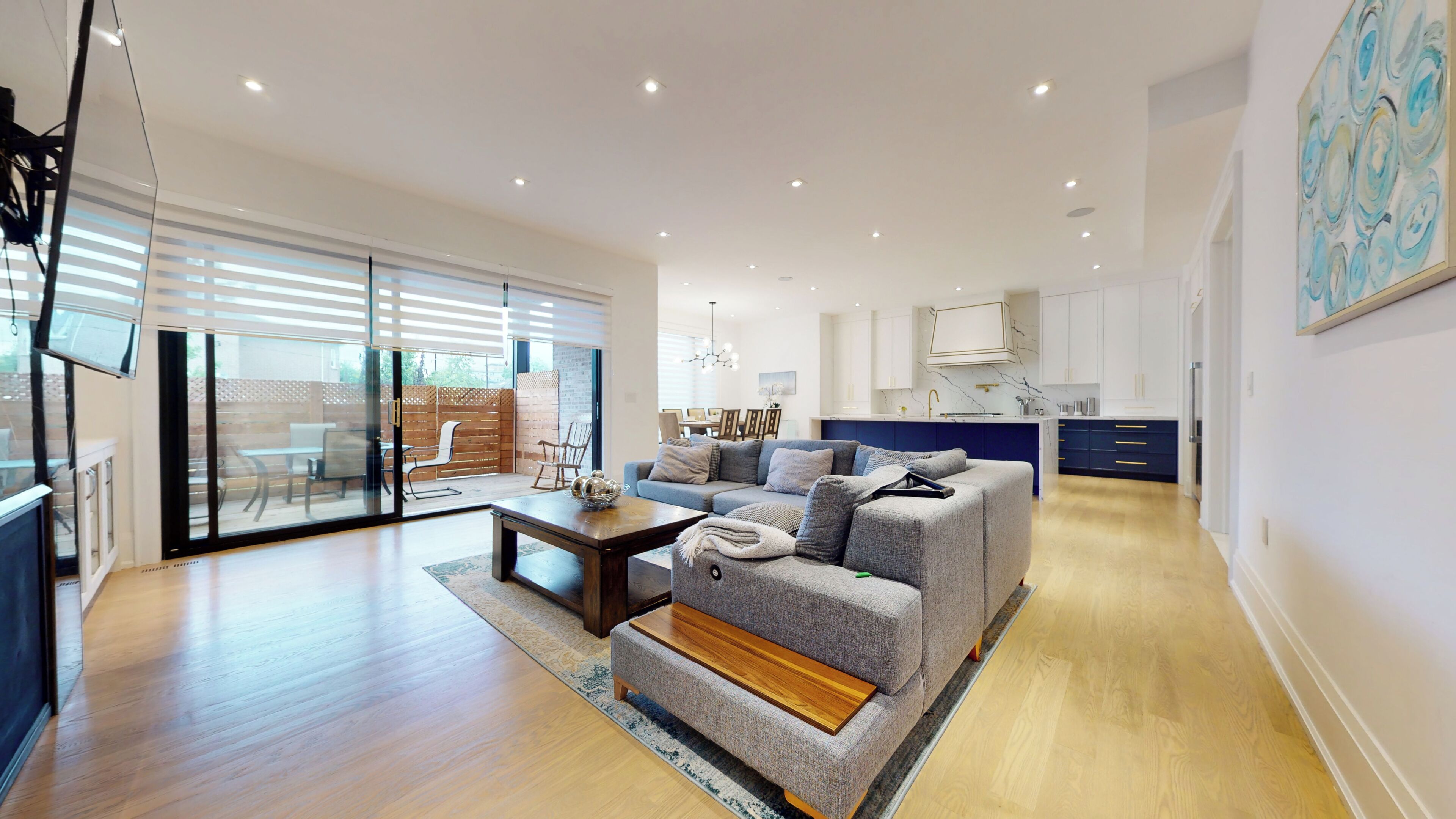 A modern living room with a sofa, a coffee table, and a TV. There is a sliding glass door leading to an outdoor area.