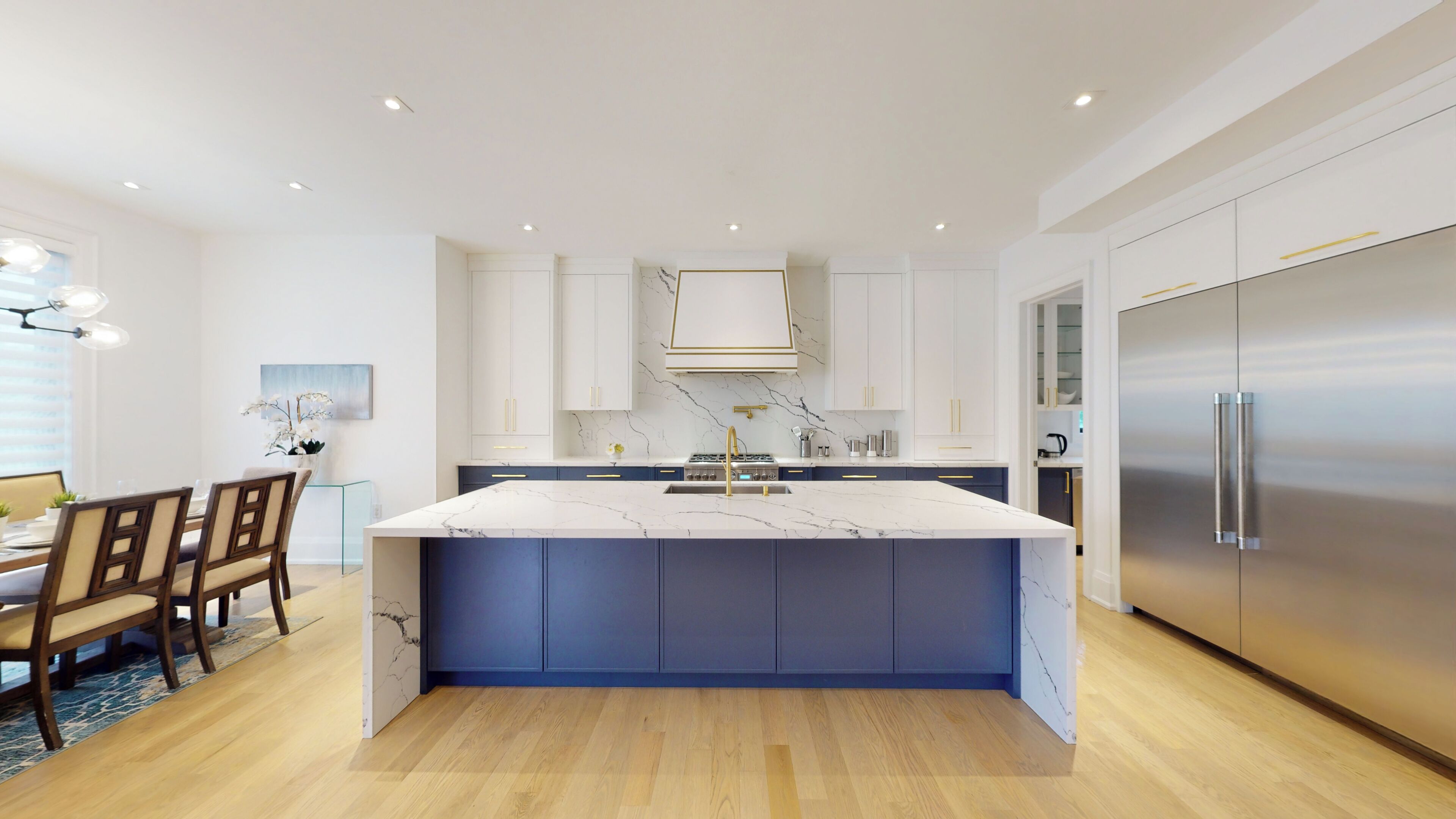 A modern kitchen with a marble island, stainless steel appliances, and a dining area with wooden chairs.