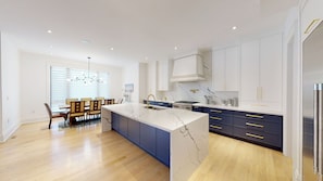 Una cocina moderna con una isla de mármol, mesa de comedor de madera e iluminación empotrada.