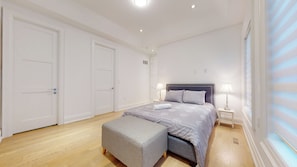 Un dormitorio con cama, dos mesitas de noche, un banco y un ventanal con persianas.